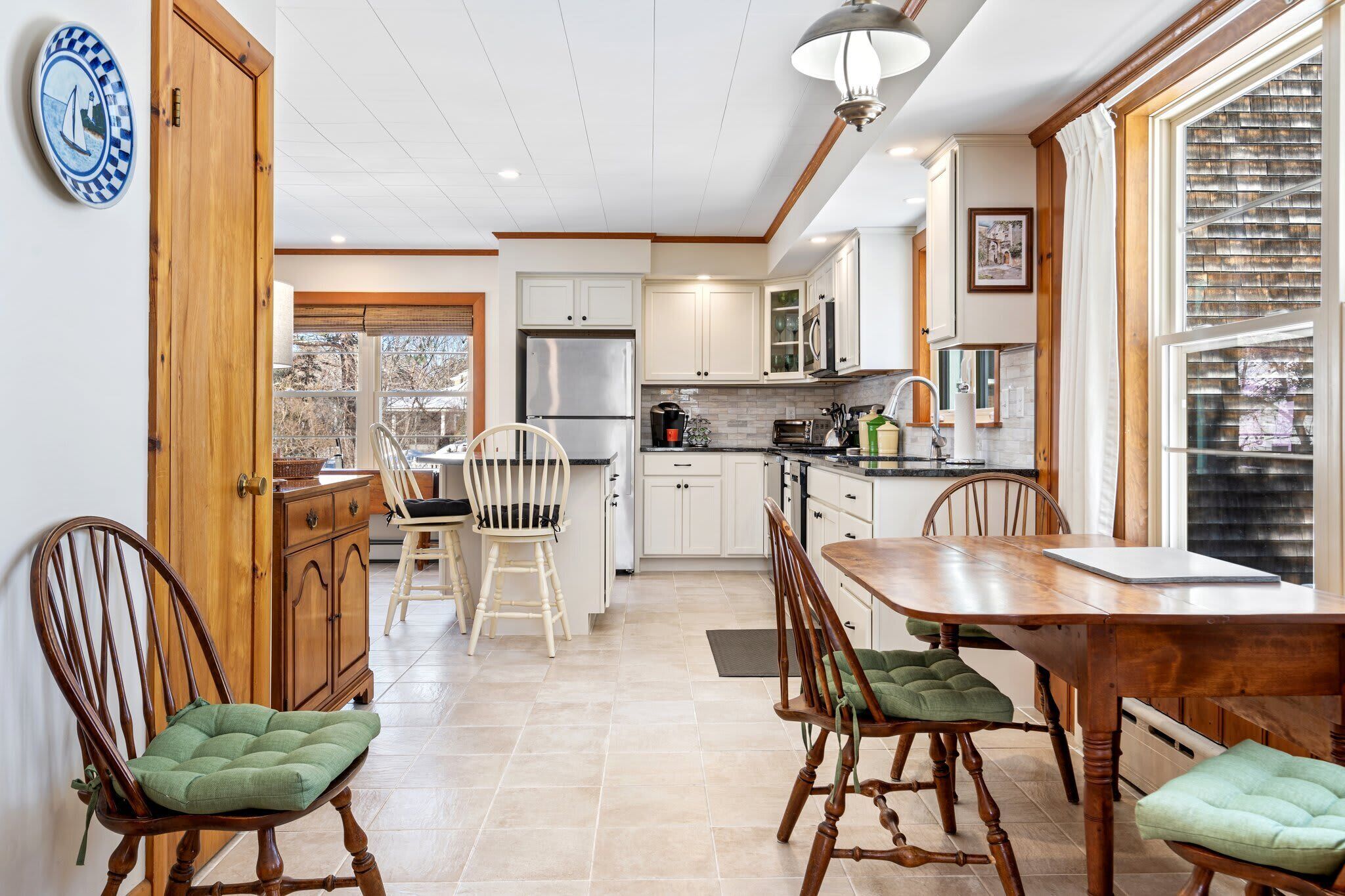 Una cocina moderna con armarios blancos, un refrigerador de acero inoxidable y un comedor con sillas y una mesa de madera.