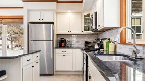 A modern kitchen with white cabinets, a stainless steel refrigerator, a granite countertop, and a sink with a modern faucet. - Bayview Beach Cottage For 4! (Saco)