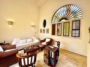 Una habitación con sofá, dos sillones, una mesita con libros y una pared decorativa con un diseño similar al sol.