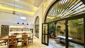 A modern kitchen with a central island, dining area with chairs, and a large glass door leading to an outdoor space with plants. - by Calamari Homes - El Porvenir (Cartagena)