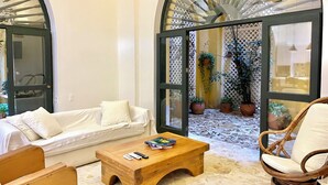 A modern living room with a white sofa, a wooden coffee table, and a wicker chair. There are potted plants and a glass door leading to a balcony. - by Calamari Homes - El Porvenir (Cartagena)