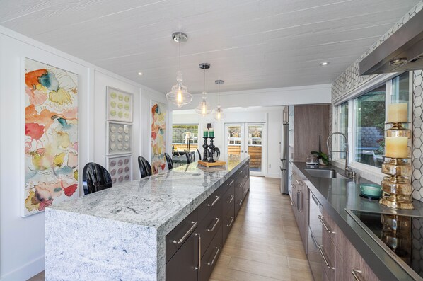 A modern kitchen with a large island, pendant lighting, and a view to the dining area.