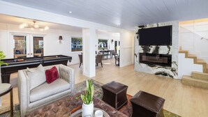 A spacious living area with a pool table, a sofa, a television mounted on a marble wall, and a staircase leading to another level. - Tranquil Home in Coto de Caza (Coto de Caza)