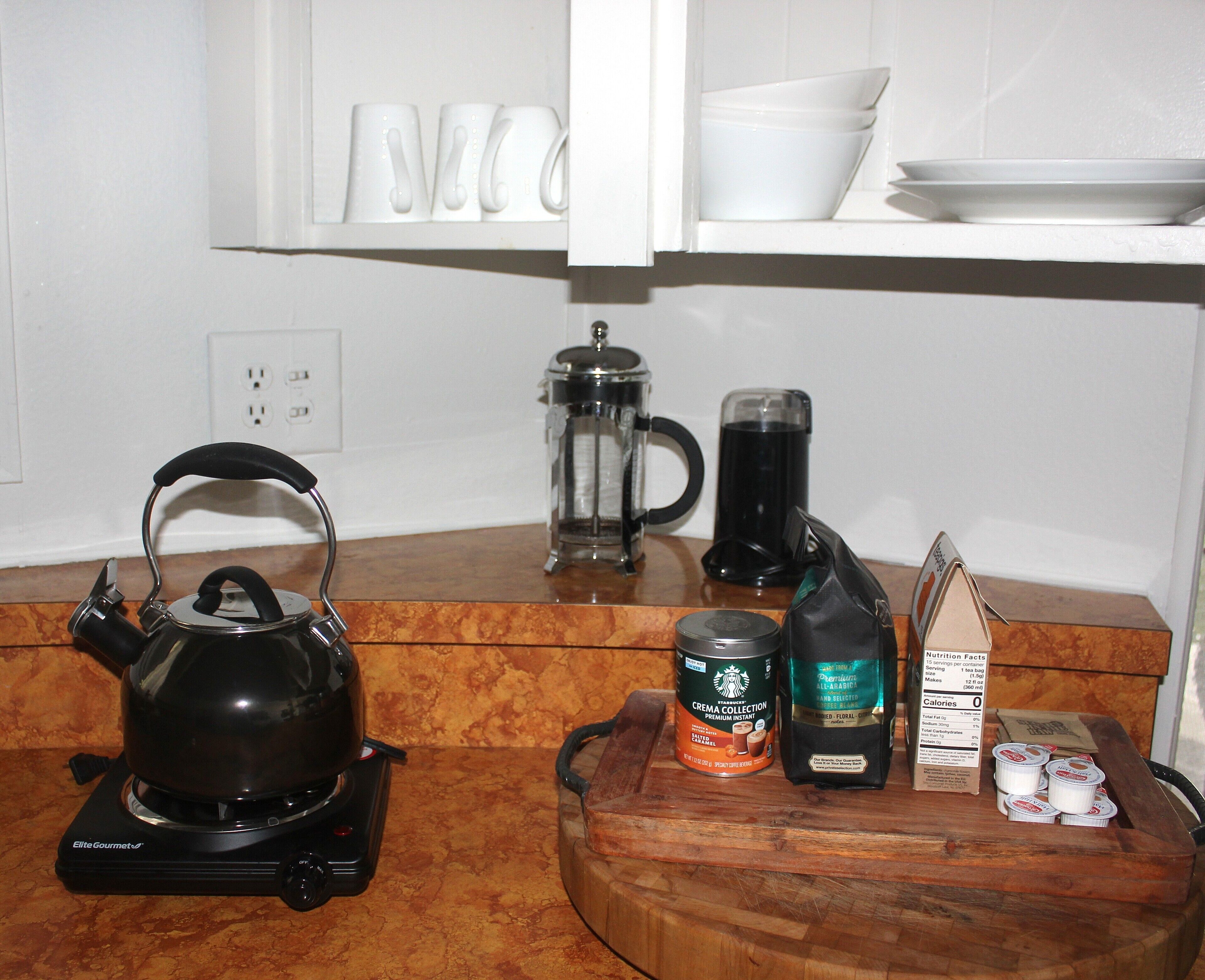 Una encimera de cocina con tetera, cafetera, jarra de leche y bolsitas de té.
