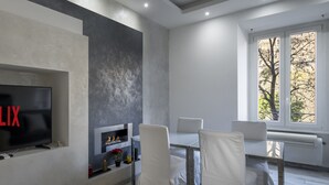 A modern living room with a flat-screen TV, fireplace, and a dining area with white chairs.