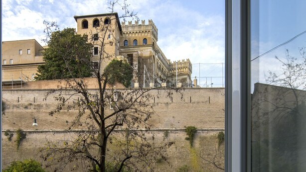 A view of a historic building with a fortified wall and a tree in the foreground.