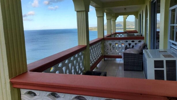 Un balcon avec vue sur l’océan, doté d’un climatiseur blanc et d’un coin salon agrémenté d’un coussin.