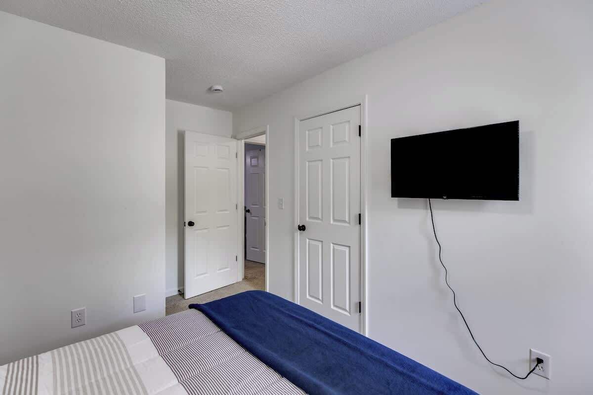A bedroom with a bed, a television mounted on the wall, and a door leading to another room.