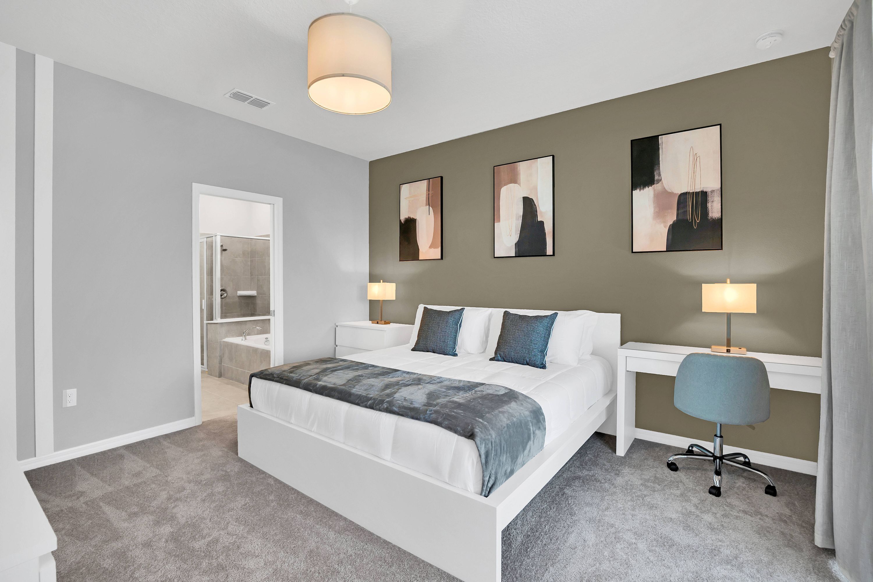 Une chambre moderne avec un grand lit, des tables de chevet, un bureau et une chaise. Les murs sont ornés de tableaux abstraits et le plafond est éclairé par un luminaire.