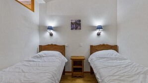 Ett litet, rent rum med två enkelsängar, trägavlar och två väggmonterade lampor.