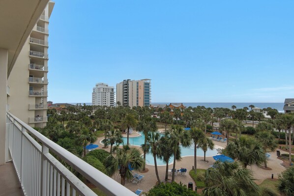 A resort with a pool area surrounded by palm trees, a view of the ocean, and high-rise buildings in the background. - "Salty Beach" Beachfront Paradise, your Dream Getaway. Poolside Cabana Bar/Cafe (Destin)