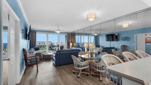A spacious living room with a large sofa, a dining table with chairs, and a balcony with a view of the ocean.