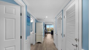 A hallway with white doors and blue walls, leading to a room with a view of houses.
