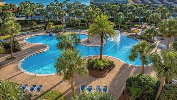 A resort with a large pool area, palm trees, and a view of the ocean.