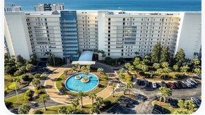 A hotel with a swimming pool, parking area, and a view of the ocean.