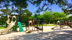 Un parque infantil con diversas estructuras de juego, incluyendo toboganes y zonas de escalada, rodeado de árboles y suelo de arena.