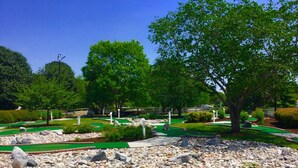 Un campo de mini golf con varios hoyos, césped artificial verde y rocas dispersas.