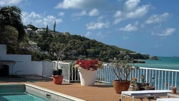 A swimming pool with a wooden deck, potted plants, and lounge chairs. - Ocean Garden Studio 2 (St Johns)