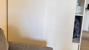 A room with a grey sofa, a white wardrobe with a hanging section, and a wooden floor. - Ocean Garden Studio 2 (St Johns)