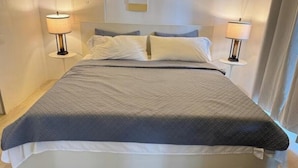A neatly made bed with a grey and white duvet, two bedside lamps, and a headboard. - Ocean Garden Studio 2 (St Johns)