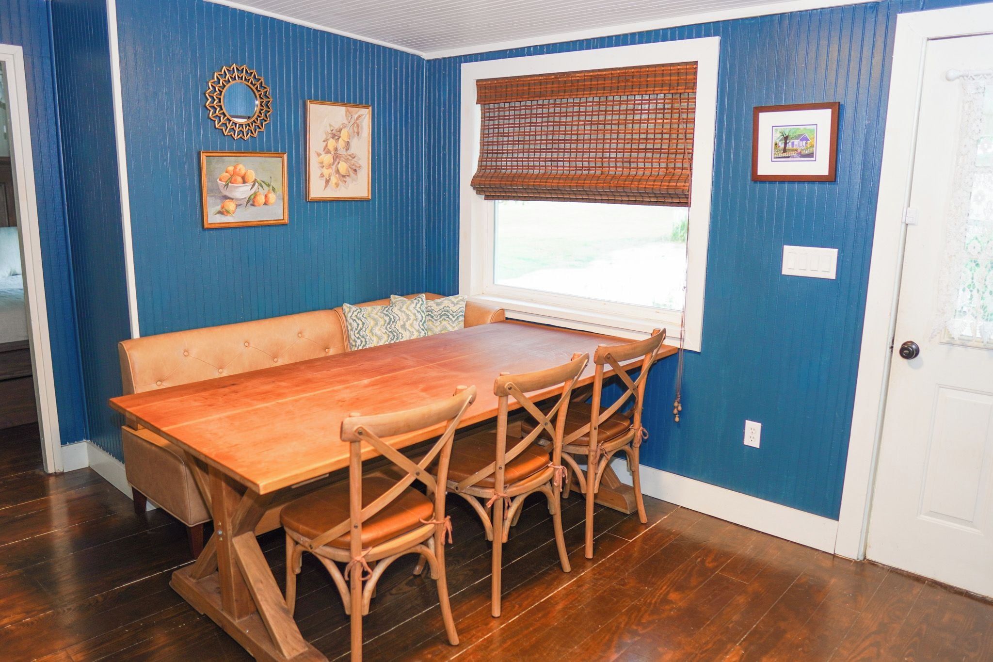 Un coin repas comprenant une table et des chaises en bois, un banc, une fenêtre avec des stores et des éléments de décoration murale.