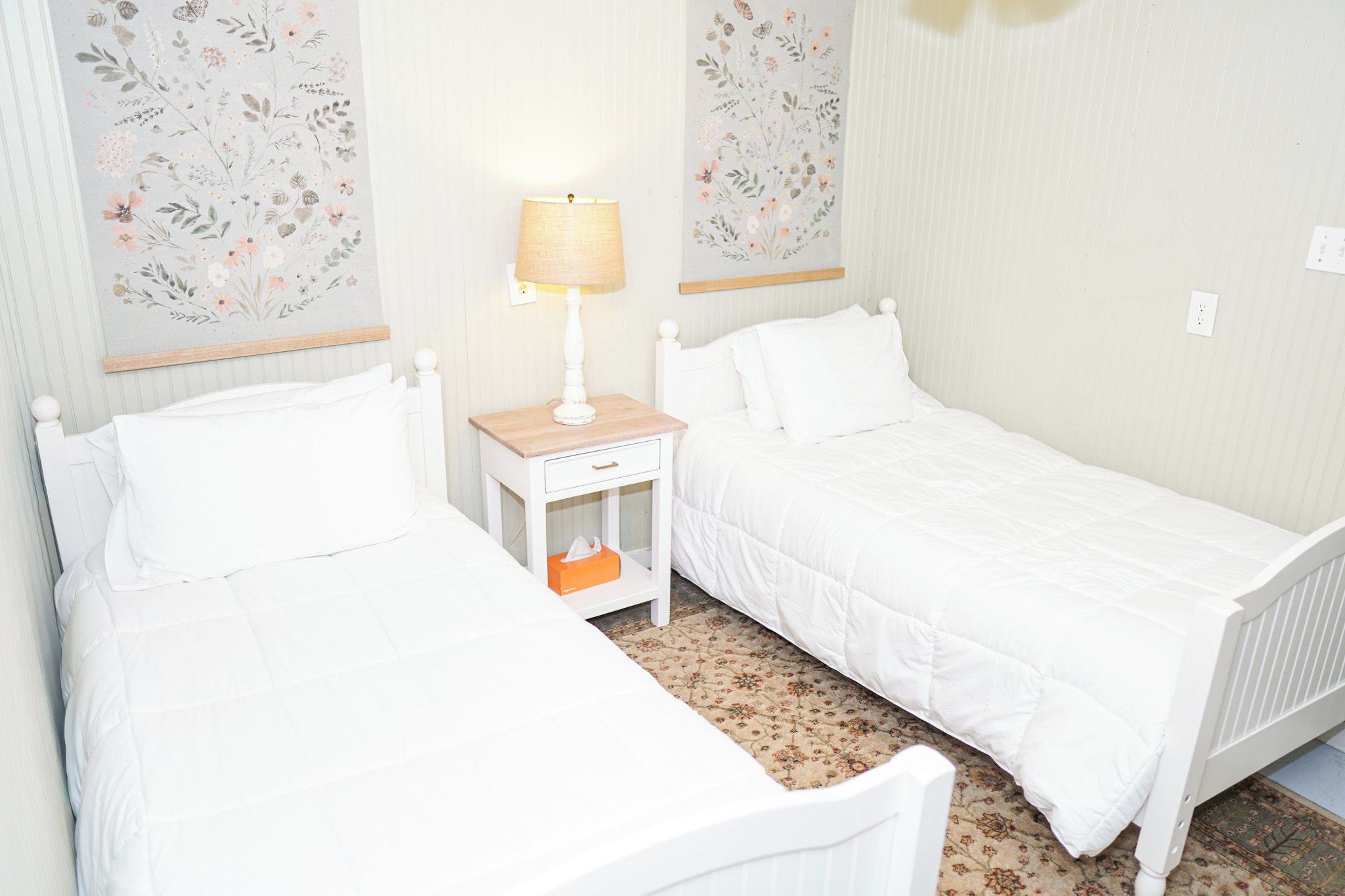 A twin room with two beds, a bedside table with a lamp, and floral wallpaper.