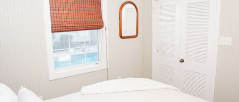 A bedroom with a bed, a window with a checkered blind, a mirror, and a set of double doors.