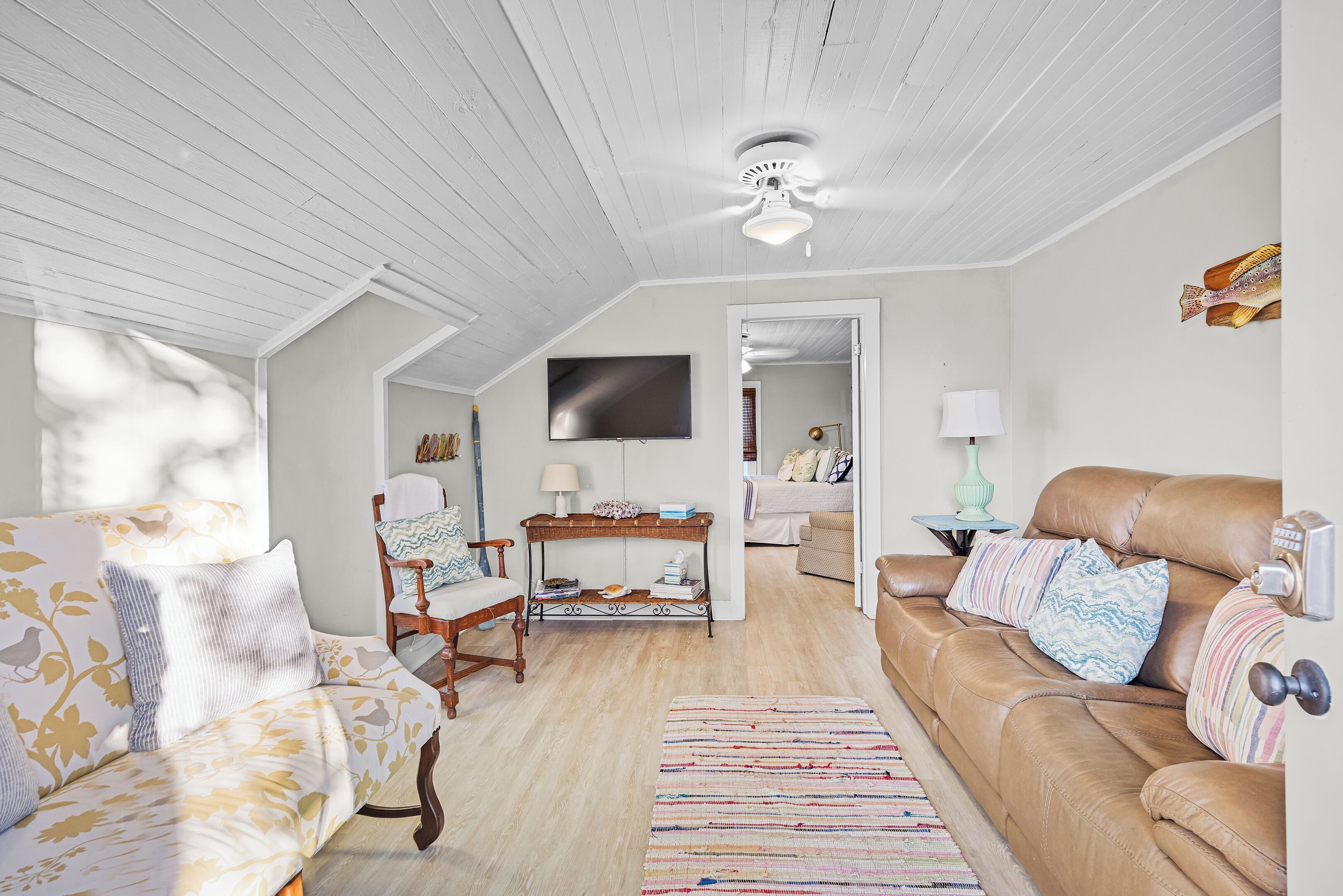 Un salon spacieux avec un plafond haut, une grande fenêtre, un ventilateur de plafond, un téléviseur, un canapé, une table basse et un tapis à motifs.