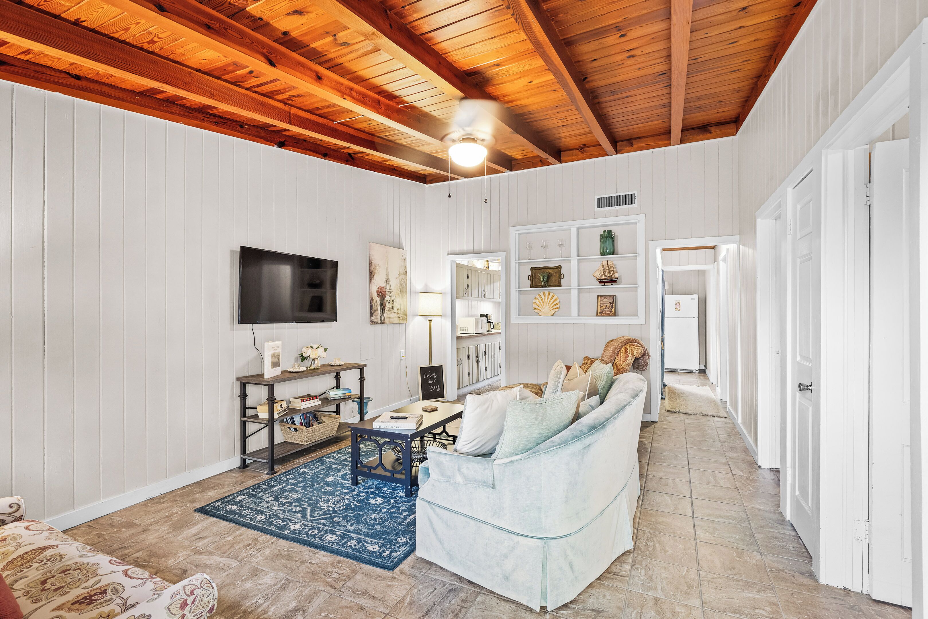 Un salon spacieux avec un canapé bleu clair, un téléviseur fixé au mur et un plafond en bois.