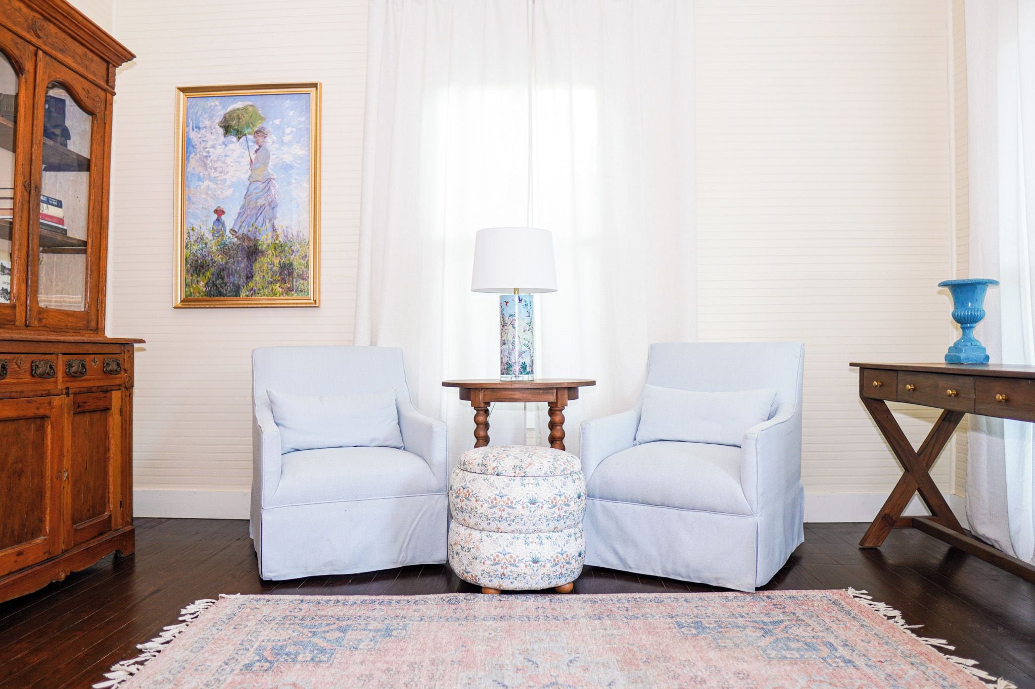 A room with two armchairs, a small table with a lamp, a cabinet, and a painting on the wall.