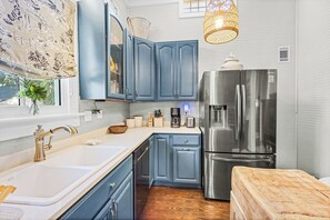 A kitchen with blue cabinets, a stainless steel refrigerator, and a wooden countertop. - Drackett House by Whiskey Properties (Bay St Louis)