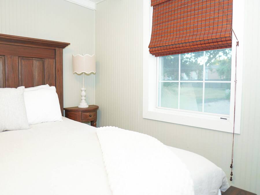 A bedroom with a large bed, a nightstand with a lamp, and a window with a red valance.