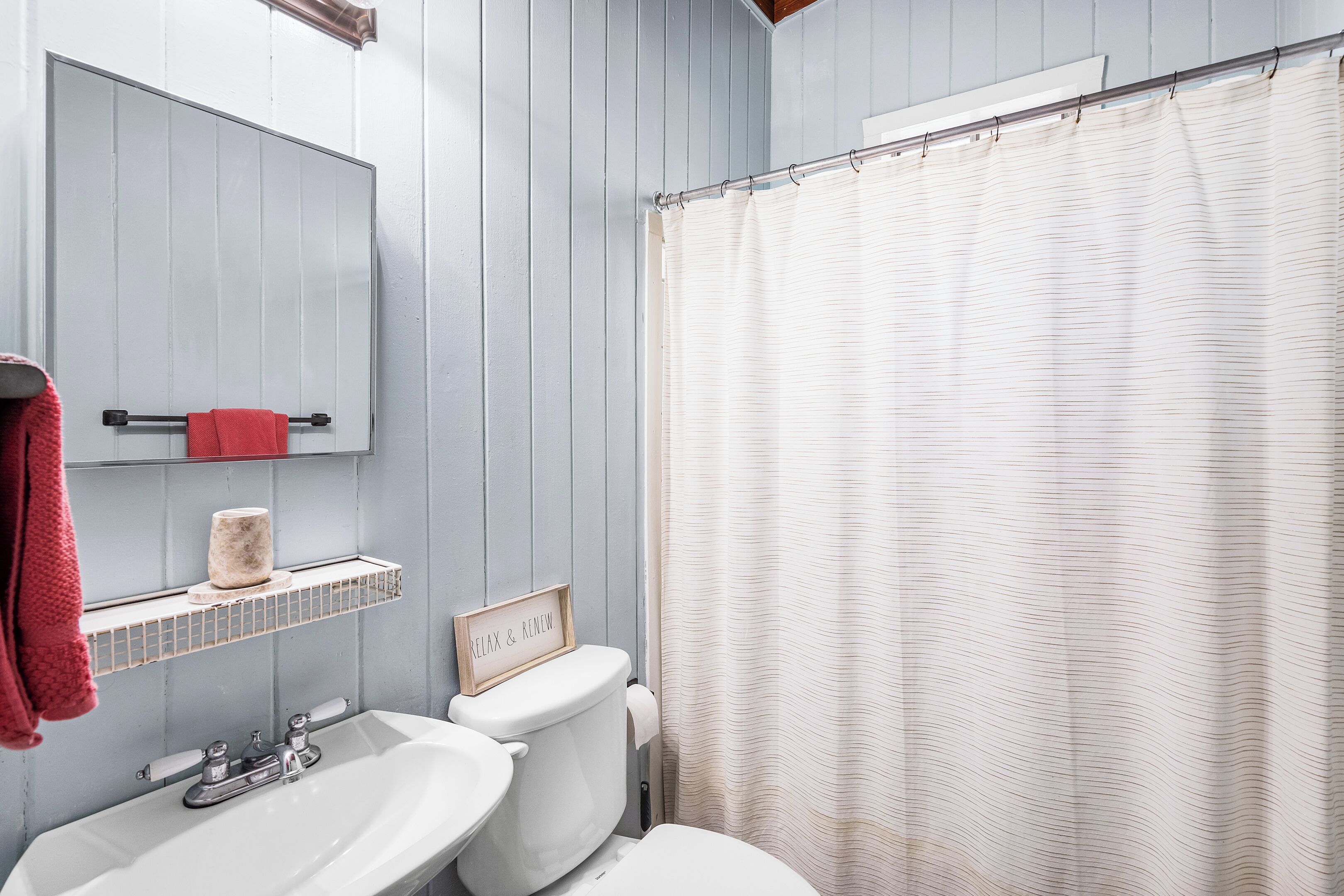 Ein Badezimmer mit einem weißen Waschbecken, einer Toilette, einem Spiegel und einer Duschvorhang.