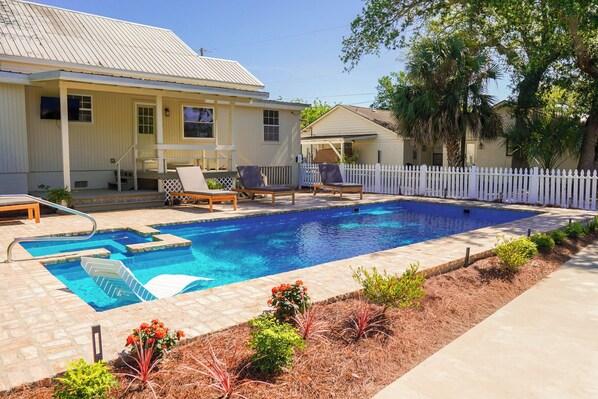 A swimming pool with a white fence, lounge chairs, and a house with a porch. - Drackett House by Whiskey Properties (Bay St Louis)