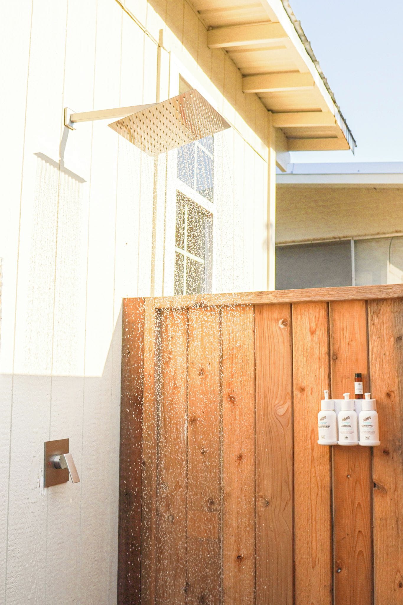 A wooden fence with a metal gate, a wooden deck, and a metal showerhead.