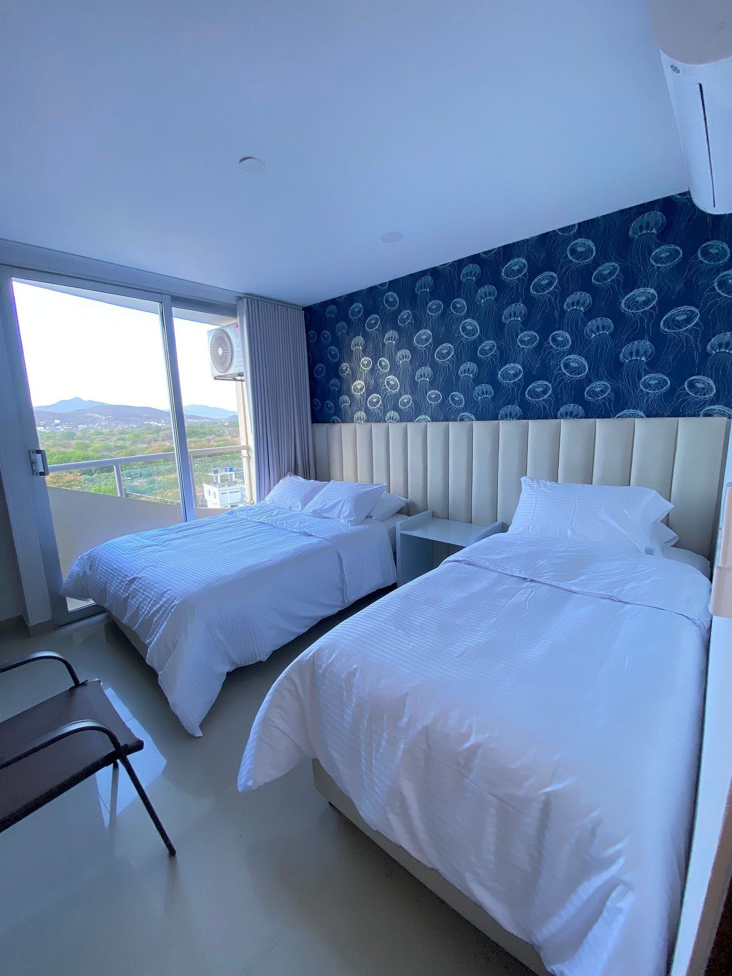Habitación de hotel con dos camas, un ventanal grande y vistas al paisaje.