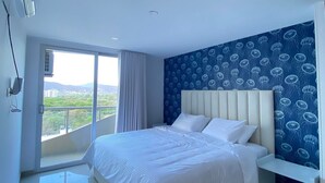 A modern bedroom with a large bed, a nightstand, a window with a view, and a ceiling fan. - U-GO Edificio Oasis (Santa Marta)