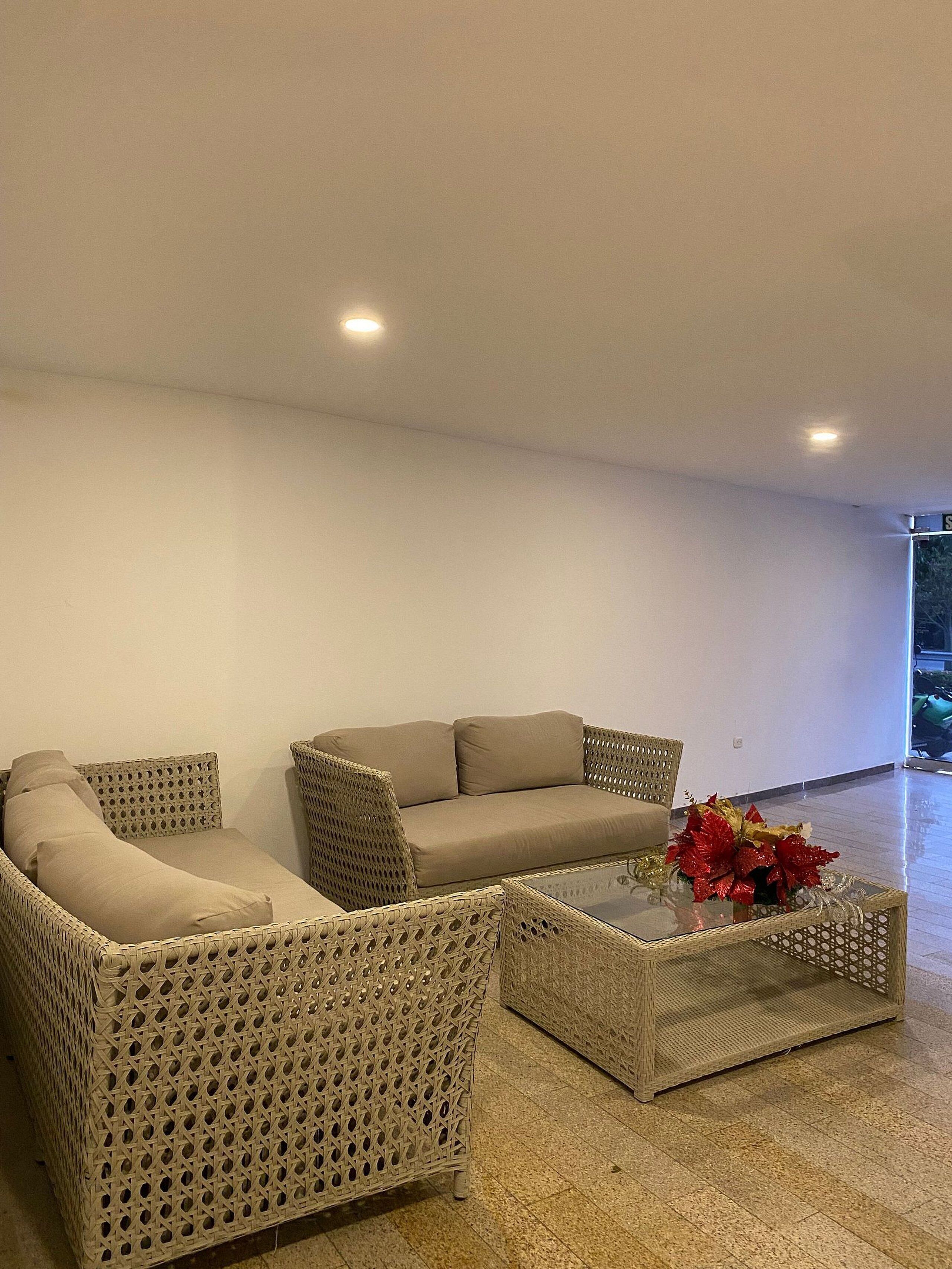 Ein modernes Wohnzimmer mit einer Eckcouch, zwei Korbstühlen und einem Glastisch mit Blumenarrangements.