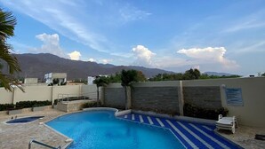 A swimming pool with a stone deck, a blue and white striped area, and a view of mountains in the background. - U-GO Edificio Oasis (Santa Marta)