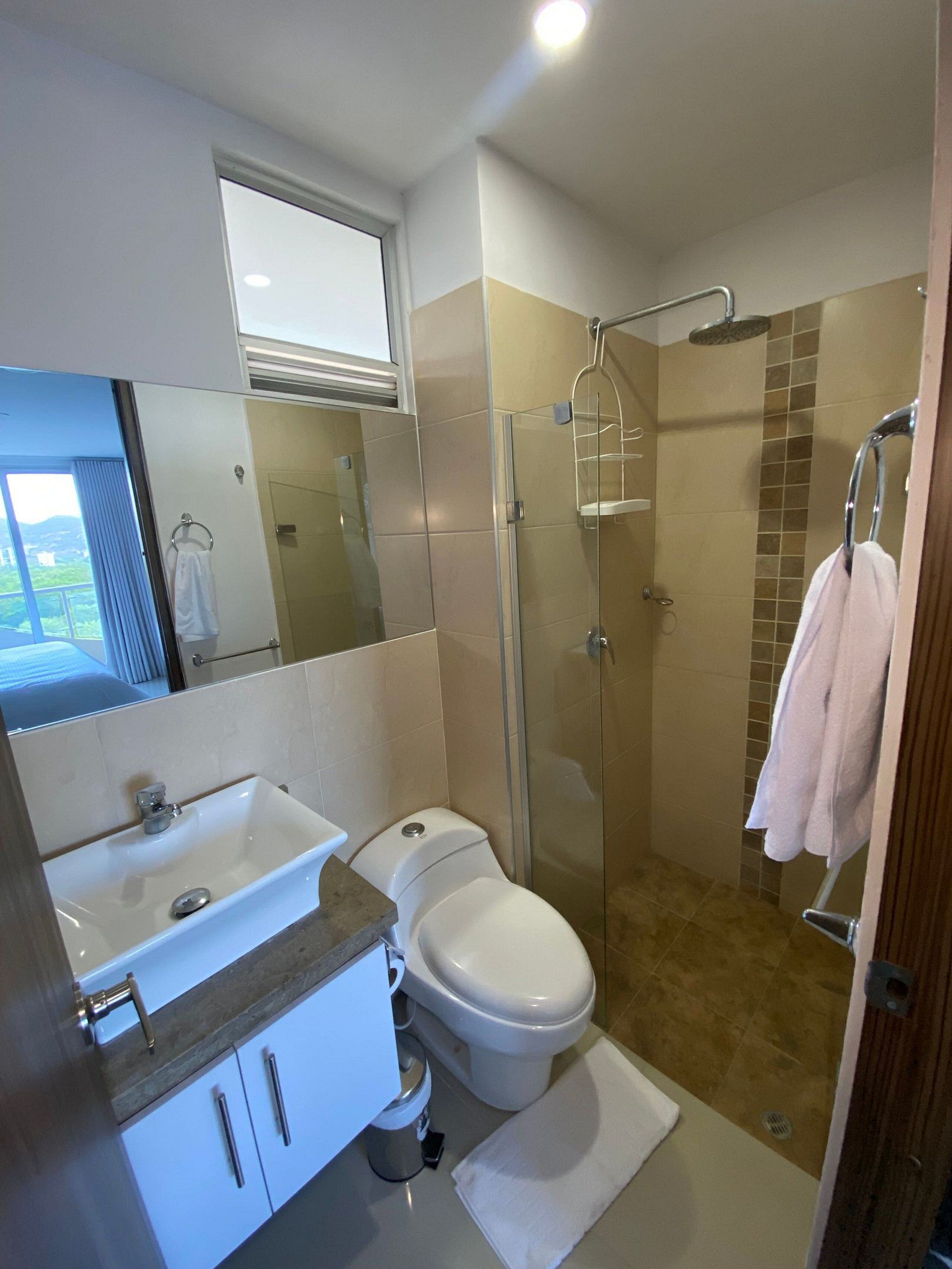 A modern bathroom with a glass-enclosed shower, a white toilet, a sink with a marble countertop, and a mirror above the sink.