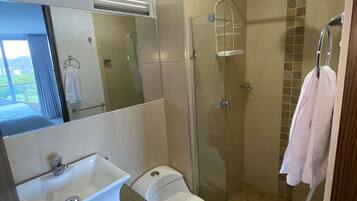 Une salle de bain moderne avec une douche à parois de verre, des toilettes blanches, un lavabo doté d'un plan de travail en marbre et un miroir au-dessus du lavabo.