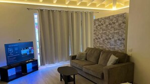 A living room with a sofa, a coffee table, and a TV on a stand. - Ocean Garden Studio I (St Johns)
