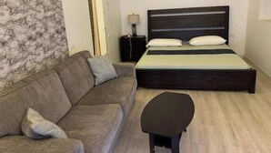 A bedroom with a dark wooden bed, a grey sofa, a small table, and a marble-patterned wall. - Ocean Garden Studio I (St Johns)