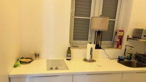 A kitchen with a white countertop, a bottle of wine, a paper towel holder, and a window with blinds. - Ocean Garden Studio I (St Johns)