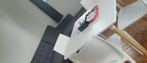 A room with a grey sofa, a white table with a red object on it, and white chairs.