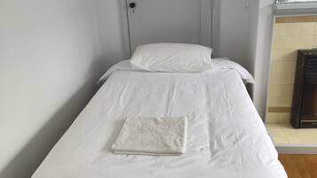 A single bed with white bedding in a room with a wooden floor and a white door.