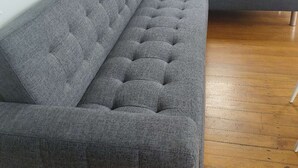 Un sofá seccional gris en una habitación con piso de madera y una ventana con cortinas.