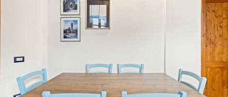 A dining area with a wooden table and six blue chairs. There are framed pictures on the wall and a light fixture above the table.