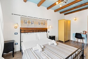 Une chambre à coucher avec une tête de lit en bois, un lit recouvert de draps blancs, un tapis à rayures, un bureau avec une chaise et une armoire.