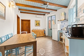 Une cuisine avec une table en bois, des chaises et un four à micro-ondes. Une porte donne accès à une autre pièce et une fenêtre offre une vue.